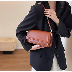 Detail view of the side accordion pleats and long leather strap on a brown shoulder bag
