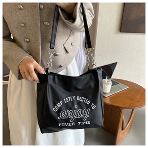 Detail of black tote bag with white slogan and stylish silver metal chain strap