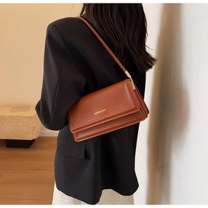 Detail of reddish-brown leather baguette bag with gold lettering and adjustable shoulder strap