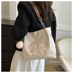 Detail of cream tote bag with pink embroidery and cute peach plush charm on handle