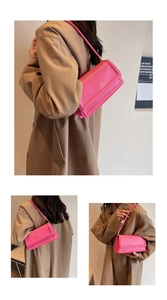 Detail view of pink leather underarm bag featuring metal logo and layered shoulder strap