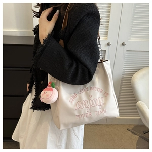 Close-up of cream tote bag with pink embroidery, silver chain, and plush charm detail