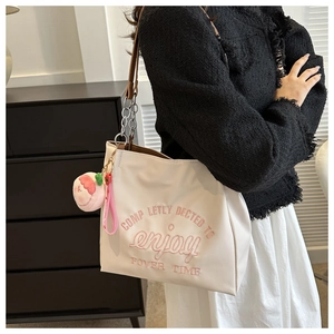 Close-up of white tote bag featuring pink embroidery and peach plush charm detail