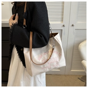 Detail of white tote bag featuring pink embroidery, brown leather straps and silver chain