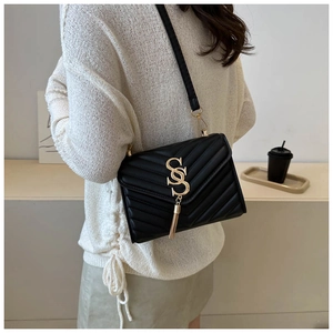 Detail of black quilted shoulder bag with gold S-buckle and elegant long tassel charm