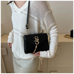 Close-up of black quilted shoulder bag with golden V-shaped stitching and tassel detail