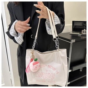 Detail of white canvas tote bag with pink embroidery and peach plush pendant accessory