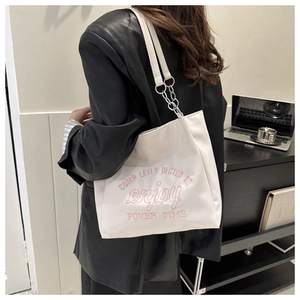 Close-up of a white tote bag featuring pink letter embroidery and a silver chain strap