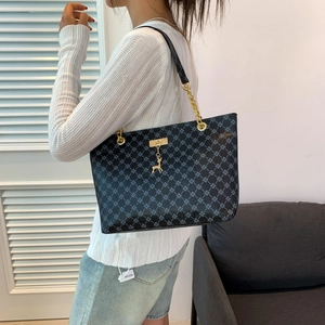 Black patterned tote bag with gold deer pendant and chain strap shown on model shoulder