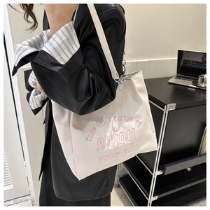 Detail of off-white canvas tote bag featuring pink embroidery and silver chain strap