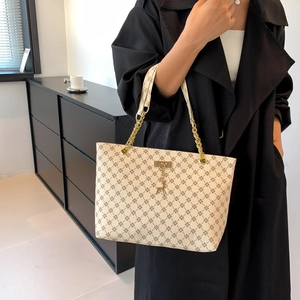 Large beige tote bag with clover pattern, gold chain strap and deer pendant on model