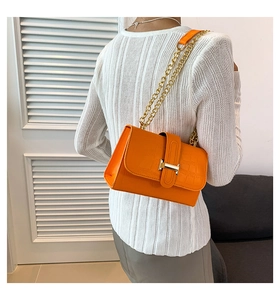 Detail view of bright orange crossbody bag with crocodile texture and gold chain strap