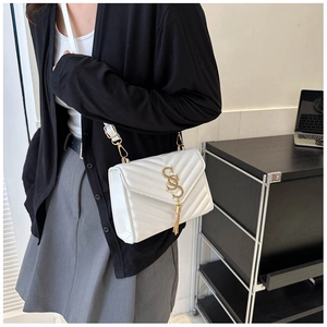 Detail of white quilted crossbody bag with golden SS logo and tassel on desk