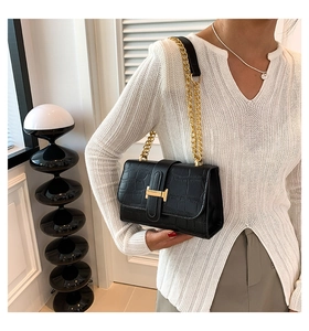 Detail shot of a black crocodile pattern shoulder bag with golden H clasp on a model