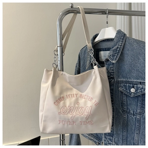 Detail of cream tote bag with pink embroidery, silver chain strap, and hung display