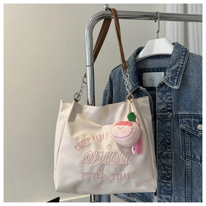 Detail of cream tote bag with pink embroidery, chain strap and peach plush charm