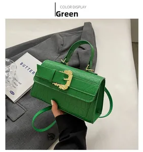 Close-up of green crocodile pattern handbag with gold baroque buckle on grey blazer