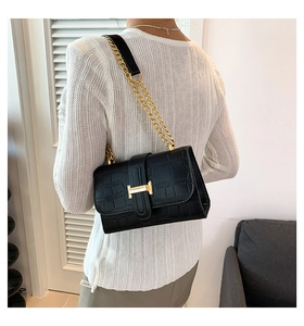 Close-up of black crocodile-embossed bag with gold H-buckle on a chain strap