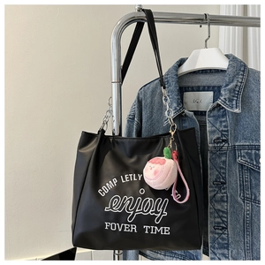 Detail of black leather tote bag with white lettering and pink peach plush charm accessory