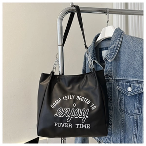 Detail of black tote bag featuring white letter embroidery and silver chain leather strap