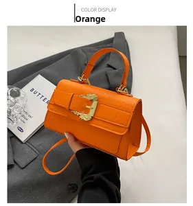 Detail of orange crocodile embossed faux leather bag with golden baroque buckle