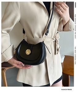 Detail of a black leather saddle bag with golden metal buckle worn by a model