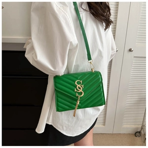 Detail of green quilted crossbody bag with golden S-shaped lock and tassel on a white shirt