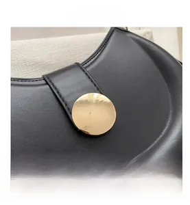 Macro view of black leather saddle bag showing gold circular buckle and stitching detail