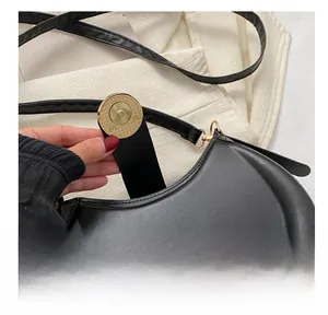 Close-up of the elegant gold magnetic buckle on a black minimalist leather saddle bag