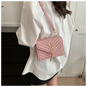 Detail view of pink quilted crossbody bag with gold metal logo and tassel on model