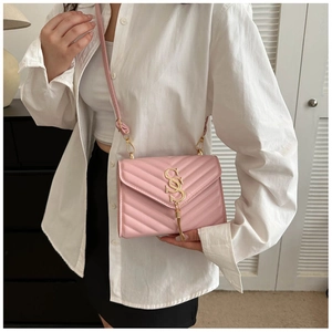 Detail of pink quilted crossbody bag with golden S logo and metal tassel on a white shirt