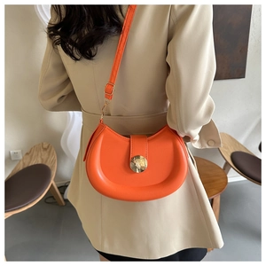 Detail of orange crescent saddle bag with gold metal buckle on a beige coat