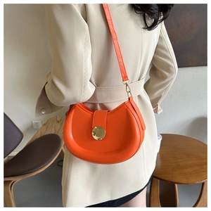 Detail of a bright orange leather half-moon saddle bag with a golden circular buckle