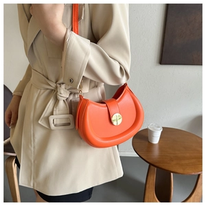 Detail of stylish orange saddle bag featuring a gold buckle on a model's beige coat