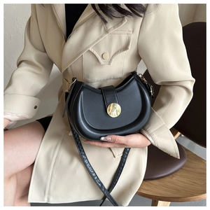 Detail view of a black leather crescent saddle bag with a round gold magnetic buckle