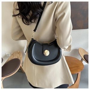 Detail of a black semi-circular saddle bag with a large gold metal buckle on a model