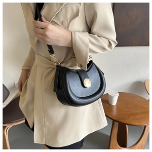 Detail of black semi-circle saddle bag with gold metal buckle on beige trench coat