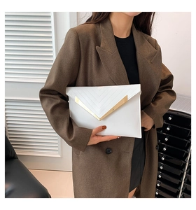 Détail d'une pochette enveloppe en cuir blanc avec surpiqûres en V et garniture métallique dorée