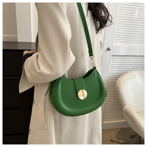 Detail of a bright green half-moon saddle bag with a round gold buckle on a model