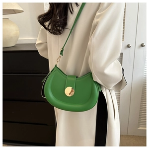 Detail of vibrant green crescent saddle bag with gold metal buckle on white coat