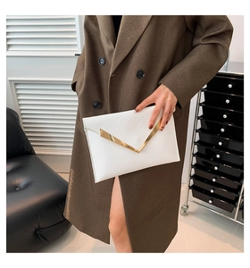 Détail d'une pochette enveloppe blanche avec bordure dorée en V et texture de couture en V