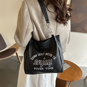 Retro black leather tote bag with white embroidery and chain strap worn by a model