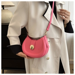 Pink crescent saddle bag with gold circular buckle worn over a beige trench coat