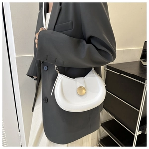 Detail of white saddle bag with golden circular magnetic clasp worn with a grey blazer