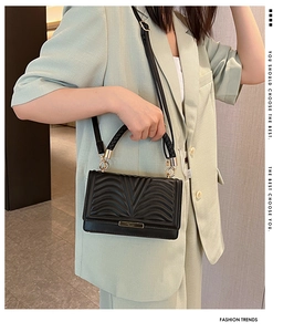 Detail of black quilted crossbody bag with textured V-pattern and gold metal clasp