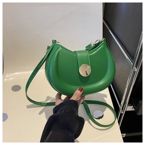 Close-up of bright green crescent saddle bag featuring a gold round buckle and PU texture
