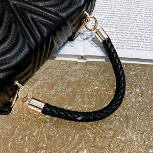 Detail of woven leather handle and gold metal rings on black quilted handbag