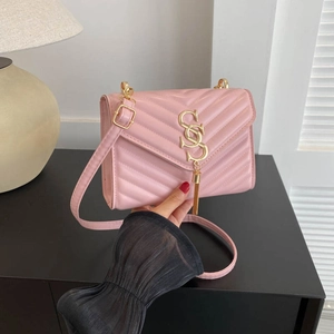 Pink quilted crossbody bag with V-stitch design and gold chain strap in hand