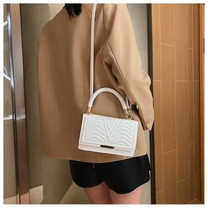 Detail of white quilted crossbody bag with golden hardware and woven handle