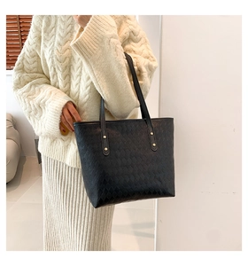 Detail of black quilted tote bag featuring golden studs and slender shoulder strap texture